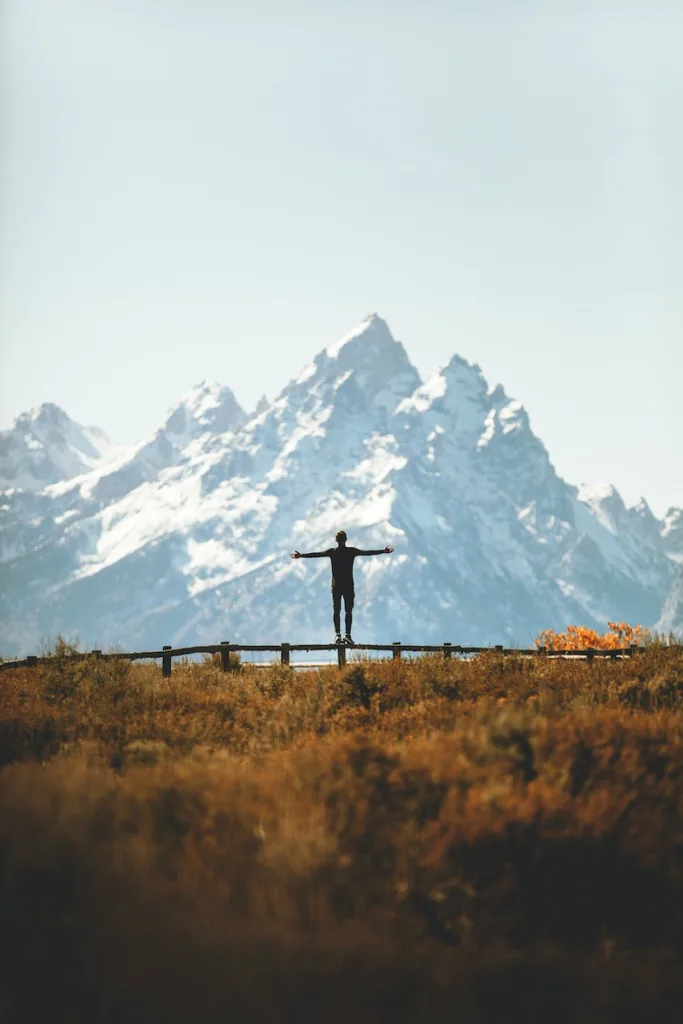 ultimate escape, man standing on fence overlooking mountain range