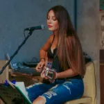 woman playing guitar while singing in backyard shed recording studio
